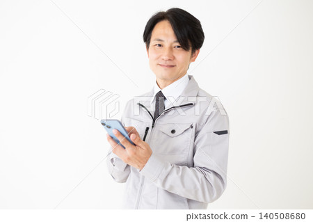 一位身穿灰色工作服的中年商務人士手持智慧型手機，背景為白色。 140508680