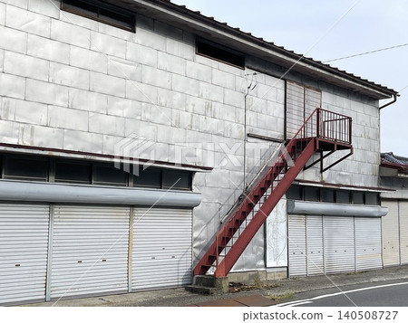Exterior view of an old warehouse building with an external staircase and shutters. 140508727
