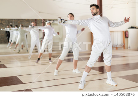 man in white fencing uniform standing with sword in hand man in white fencing uniform standing with sword in hand 140508876