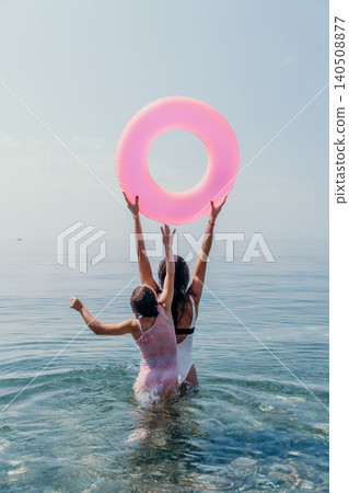 Mother daughter ocean enjoying a sunny beach day while playing in the water with a bright pink inflatable ring during their summer vacation Mother daughter ocean enjoying a sunny beach day while playing in the water with a bright pink inflatable ring during their summer vacation 140508877
