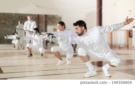 Men and women in white uniforms practice fencing techniques with foils in hands Men and women in white uniforms practice fencing techniques with foils in hands 140509009