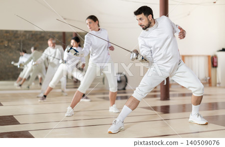 Men and women practicing epee moves in gym Men and women practicing epee moves in gym 140509076