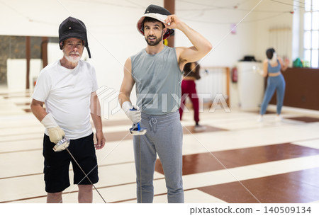 Portrait of an elderly coach with rapier in his hands and atletic man during fencing training in gym Portrait of an elderly coach with rapier in his hands and atletic man during fencing training in gym 140509134