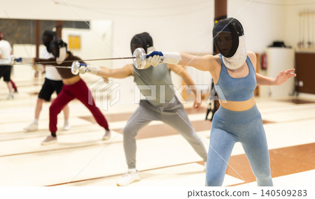 Men and women in fencing masks practicing epee moves Men and women in fencing masks practicing epee moves 140509283
