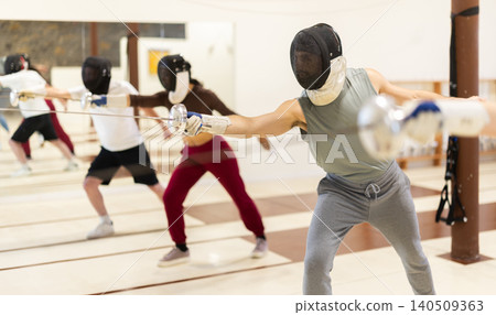 Men and women in fencing masks practicing epee moves Men and women in fencing masks practicing epee moves 140509363