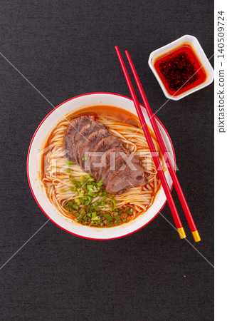 Chinese spicy beef noodle soup served with red chopsticks and chili oil, dark background Chinese spicy beef noodle soup served with red chopsticks and chili oil, dark background 140509724