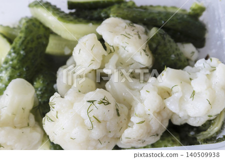 Close-up of pickled cauliflower florets and crunchy green cucumbers seasoned with fresh green dill in a plastic container. Healthy homemade fermented vegetables appetizer. Close-up of pickled cauliflower florets and crunchy green cucumbers seasoned with fresh green dill in a plastic container. Healthy homemade fermented vegetables appetizer. 140509938