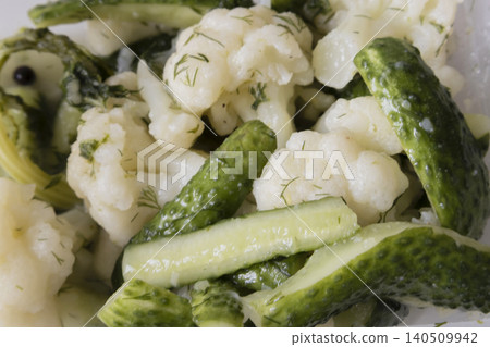 Close-up of pickled cauliflower florets and crunchy green cucumbers seasoned with fresh green dill in a plastic container. Healthy homemade fermented vegetables appetizer. 140509942