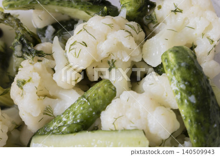 Close-up of pickled cauliflower florets and crunchy green cucumbers seasoned with fresh green dill in a plastic container. Healthy homemade fermented vegetables appetizer. Close-up of pickled cauliflower florets and crunchy green cucumbers seasoned with fresh green dill in a plastic container. Healthy homemade fermented vegetables appetizer. 140509943