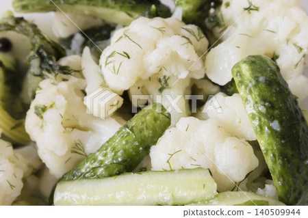 Close-up of pickled cauliflower florets and crunchy green cucumbers seasoned with fresh green dill in a plastic container. Healthy homemade fermented vegetables appetizer. Close-up of pickled cauliflower florets and crunchy green cucumbers seasoned with fresh green dill in a plastic container. Healthy homemade fermented vegetables appetizer. 140509944