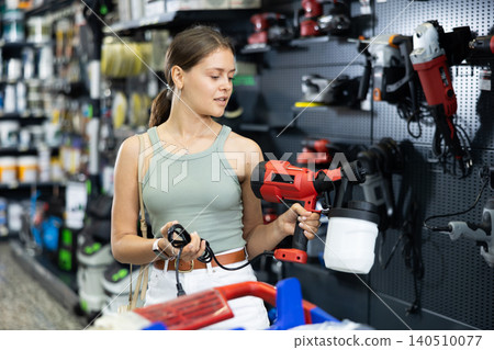 Woman choose examines spray gun airbrush in tools department of construction store 140510077