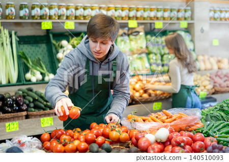 Young male seller holding tomatoes standing by counter in grocery market Young male seller holding tomatoes standing by counter in grocery market 140510093