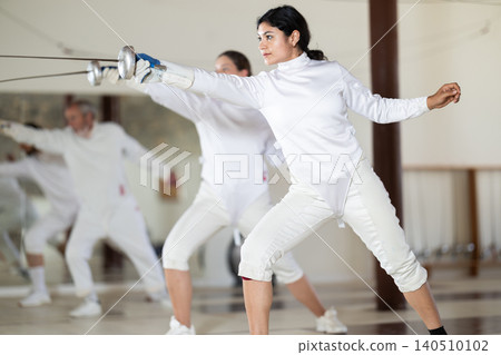 Men and women practicing epee moves in gym Men and women practicing epee moves in gym 140510102