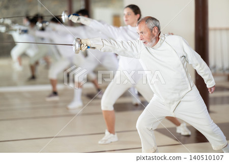 Men and women in white uniforms practice fencing techniques with foils in hands Men and women in white uniforms practice fencing techniques with foils in hands 140510107