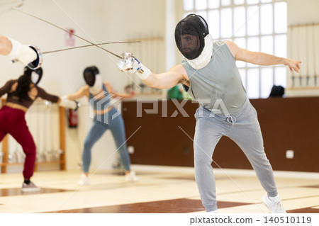 Group of fencers trains in duels and works out blows on the pillows in gym 140510119