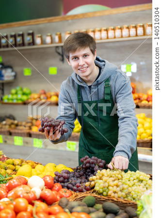 Young male seller putting pomegranates in market basket in grocery store Young male seller putting pomegranates in market basket in grocery store 140510304