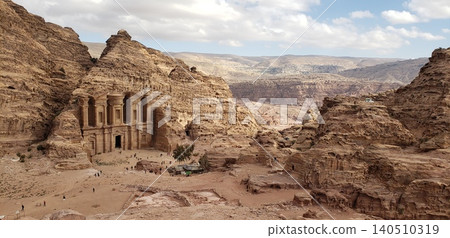 A distant view of Ad Deir, part of the Petra ruins, perched on a vast rocky mountain. A distant view of Ad Deir, part of the Petra ruins, perched on a vast rocky mountain. 140510319
