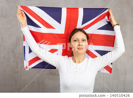 Happy young woman holding flag of Great Britain against unicoloured background Happy young woman holding flag of Great Britain against unicoloured background 140510426