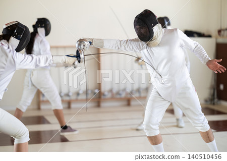 Fencing training - men and women in white uniforms practice fencing in a gymnasium for duel 140510456