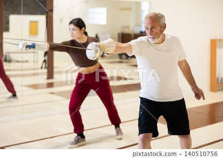 Elderly man practicing fencing movements in gym Elderly man practicing fencing movements in gym 140510756