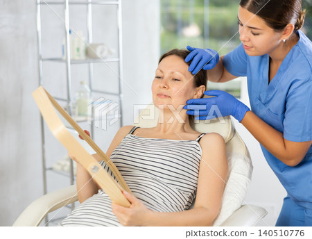 Cosmetologist examine patients contour face after lifting oval of face and palpate cheekbones 140510776