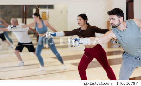 Sporty adult male fencer practicing fencing technique in training room Sporty adult male fencer practicing fencing technique in training room 140510787