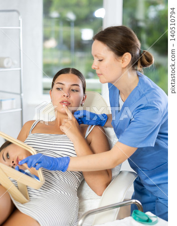 Adult female cosmetologist examining face of female patient Adult female cosmetologist examining face of female patient 140510794