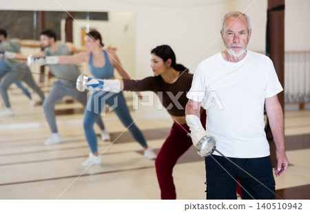 Portrait of an elderly man holding rapier during fencing training in gym Portrait of an elderly man holding rapier during fencing training in gym 140510942
