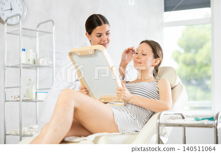 Young woman cosmetologists examines face of female patient 140511064