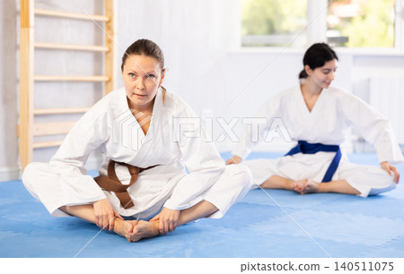 Woman in a kimono sits in a butterfly pose and practices stretching in gym Woman in a kimono sits in a butterfly pose and practices stretching in gym 140511075