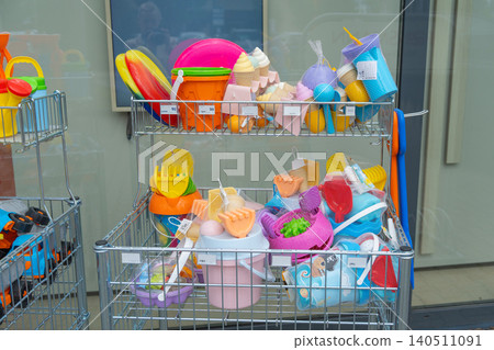 Selection of colorful plastic sand buckets, shovels and beach toys stored in metal wire baskets outside a supermarket. Children outdoor summer toys and sandbox equipment arranged on a retail display Selection of colorful plastic sand buckets, shovels and beach toys stored in metal wire baskets outside a supermarket. Children outdoor summer toys and sandbox equipment arranged on a retail display 140511091