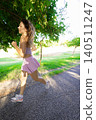 Woman runs on a path in a park during the day near trees and grassy areas 140511247