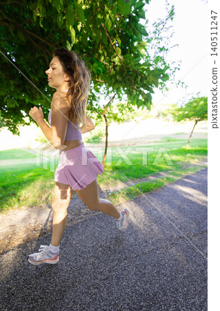 Woman runs on a path in a park during the day near trees and grassy areas Woman runs on a path in a park during the day near trees and grassy areas 140511247