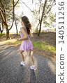 Woman runs on a path near trees during daylight in a park setting while wearing a purple outfit and sneakers 140511256