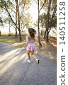 Woman runs on a path surrounded by trees during the late afternoon sunlight 140511258