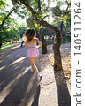 Young woman runs down a path surrounded by trees during daylight hours in a park setting 140511264