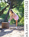 Woman ties shoelace while standing on a tree stump in a forest setting during daytime 140511282