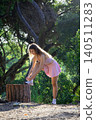 Woman ties shoelaces while standing on tree stump in forest during sunny day 140511283