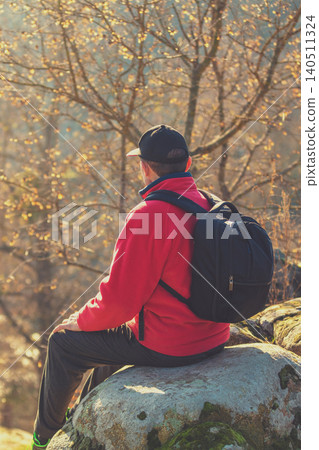 A tourist sits on a rock above a beautiful canyon on a sunny autumn day. The man looks at the river A tourist sits on a rock above a beautiful canyon on a sunny autumn day. The man looks at the river 140511324