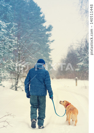 Man and dog are best friends. A man with a dog walks along the road along the forest in a snowy winter Man and dog are best friends. A man with a dog walks along the road along the forest in a snowy winter 140511448