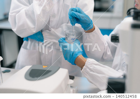 Two Asian female environmental scientists analyzing water quality samples with centrifuge and petri dish in laboratory. 140512458