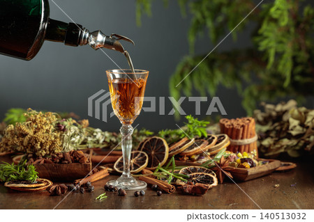 Herbal bitter liqueur is poured from a dark glass vintage bottle into a glass. Herbal bitter liqueur is poured from a dark glass vintage bottle into a glass. 140513032