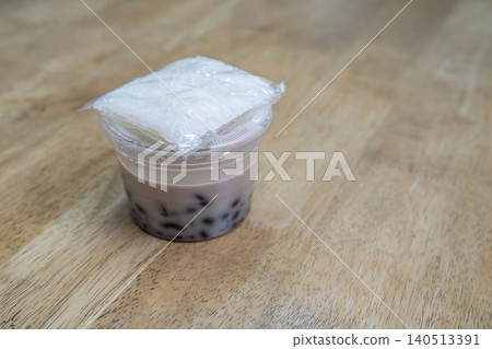 Thai dessert of black beans in sweet coconut milk served in a plastic cup with a side of sticky rice in a clear bag. Placed on a light brown wooden table in a professional stock photography style. Thai dessert of black beans in sweet coconut milk served in a plastic cup with a side of sticky rice in a clear bag. Placed on a light brown wooden table in a professional stock photography style. 140513391