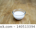 Small glass bowl filled with fresh coconut milk or cream placed on a rustic wooden table surface. High angle shot of a culinary ingredient used in cooking or skin care. Professional photography. 140513394