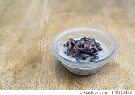 Traditional Thai dessert of black beans in sweet coconut milk served in a glass bowl on a wooden table. High angle view with copy space on the left side. Authentic Asian culinary food photography. Traditional Thai dessert of black beans in sweet coconut milk served in a glass bowl on a wooden table. High angle view with copy space on the left side. Authentic Asian culinary food photography. 140513396