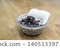 Traditional Thai dessert of black beans in sweet coconut milk served with sticky rice in a clear glass bowl on a wooden table background. Delicious Asian snack or street food concept. 140513397