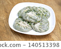 Steamed Chinese chive dumplings served on a white square plate. Translucent dough reveals fresh green garlic chive filling. Authentic Asian appetizer placed on a rustic wooden table surface. 140513398