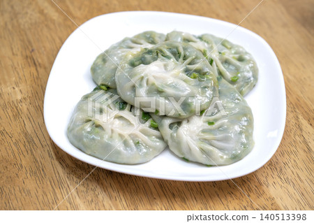 Steamed Chinese chive dumplings served on a white square plate. Translucent dough reveals fresh green garlic chive filling. Authentic Asian appetizer placed on a rustic wooden table surface. Steamed Chinese chive dumplings served on a white square plate. Translucent dough reveals fresh green garlic chive filling. Authentic Asian appetizer placed on a rustic wooden table surface. 140513398
