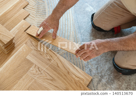 Carpenter installing herringbone wooden parquet planks during flooring work in apartment renovation Carpenter installing herringbone wooden parquet planks during flooring work in apartment renovation 140513670