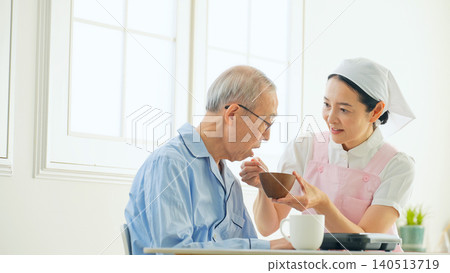 A female care worker assists an elderly man with his meal. A female care worker assists an elderly man with his meal. 140513719